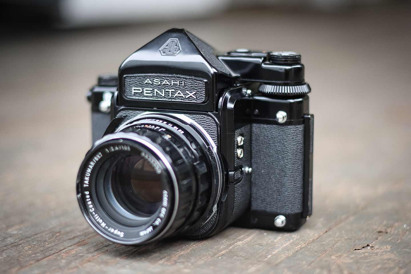 Large black camera with a lens attached, Asahi Pentax embossed on the front, a large dial on the top right side, and knobs and silver accessory mounts